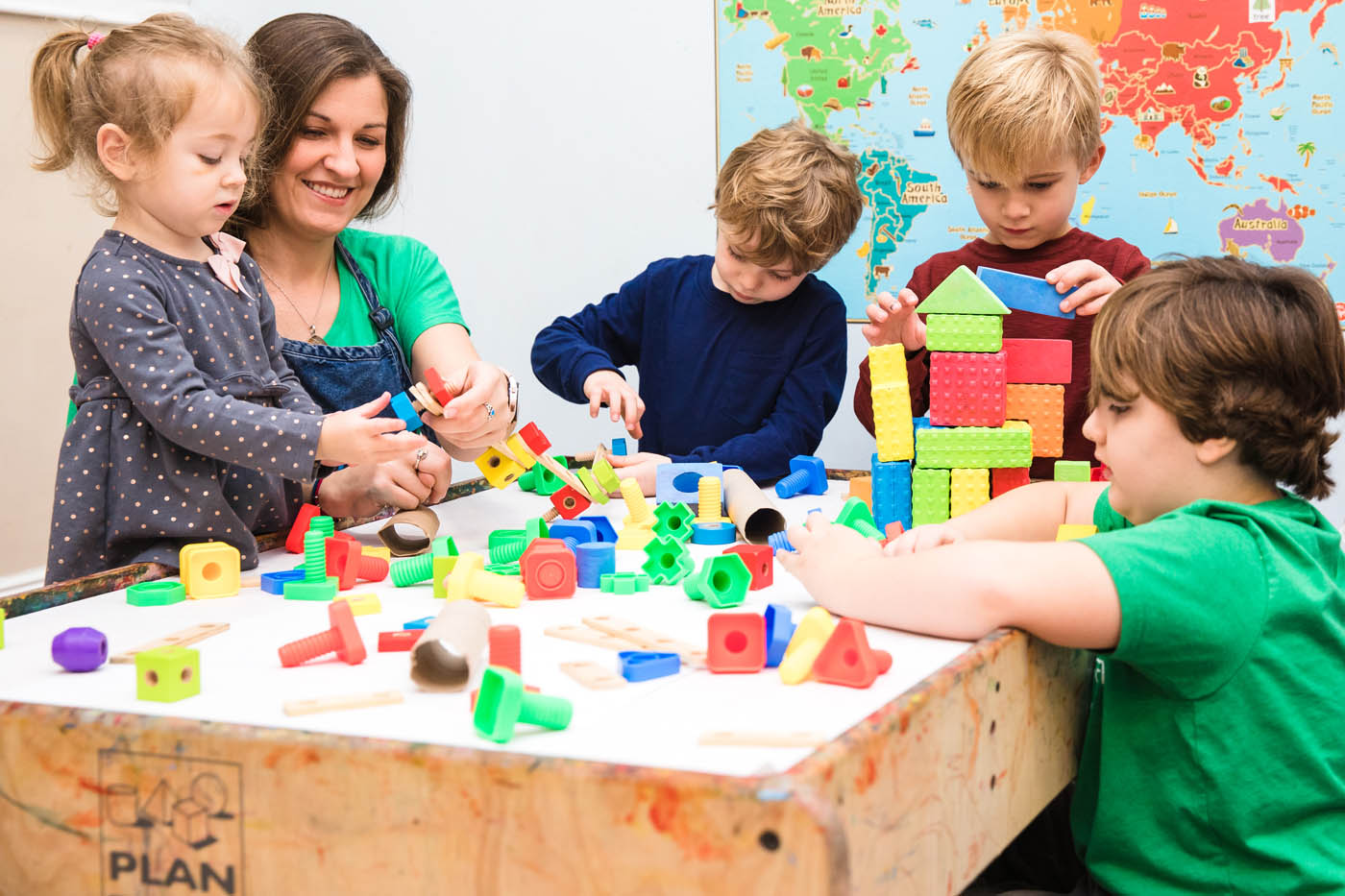 A teacher at Kids Garden playing with building blocks with a group of kids.